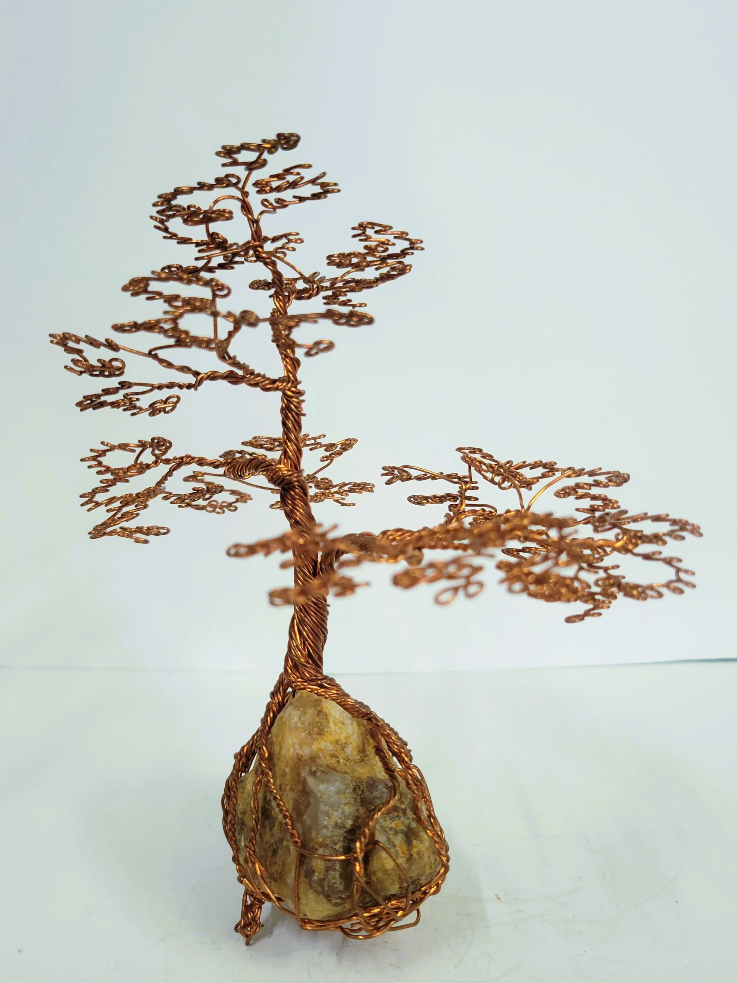A miniature tree sculpture made of twisted copper wire with a rock as its base.