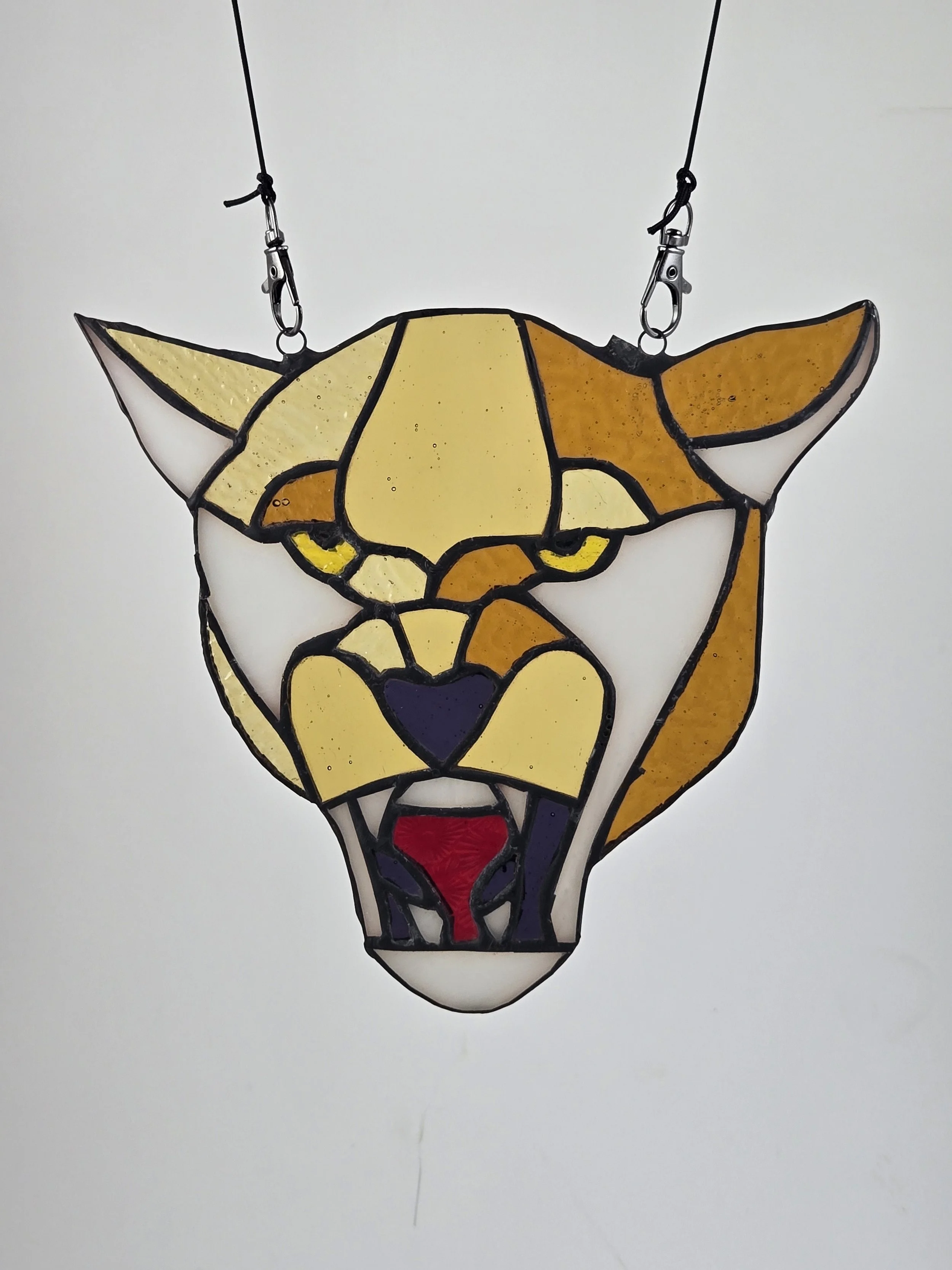 A stained glass art piece of a panthers face with yellow, white, tan, black, and red glass pieces.