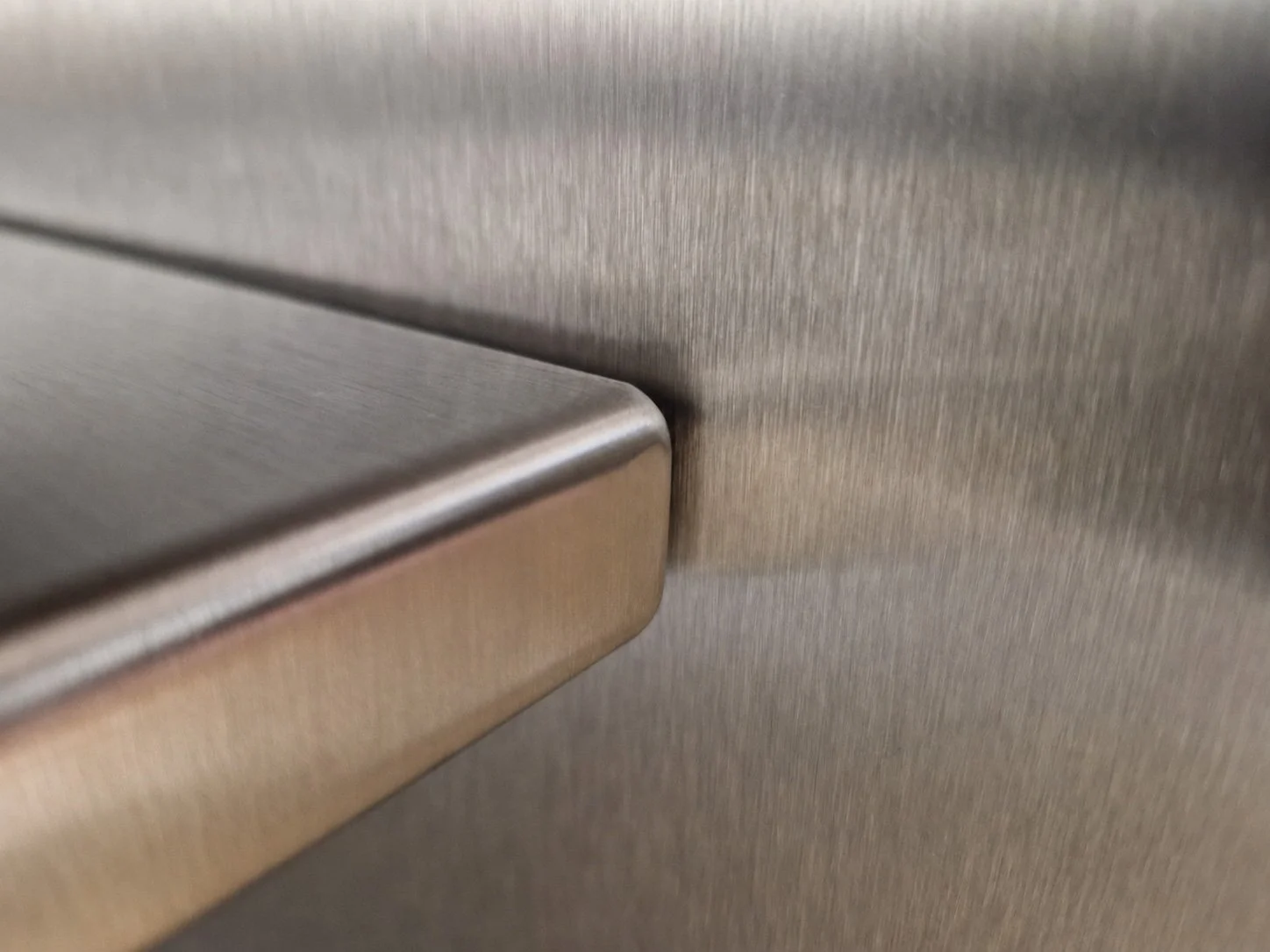 Close-up view of a metallic appliance, possibly a refrigerator or oven, with a textured brushed metal surface and a rounded edge.