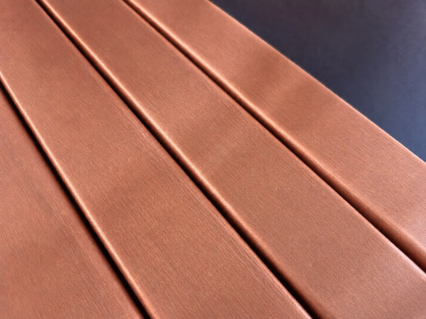 Close-up of brown wooden or composite outdoor furniture slats, with a dark background.