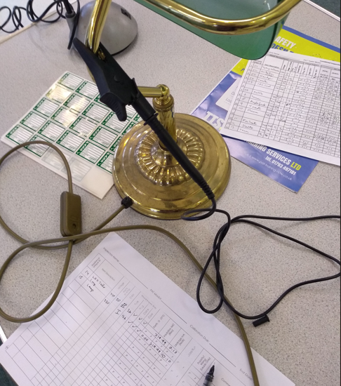 Office desk with a brass lamp, a power strip, documents, and electronic cords.