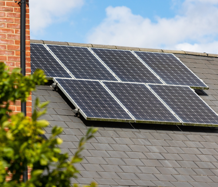 Solar panels installed on a house roof with a cloudy sky and a tree in the foreground.