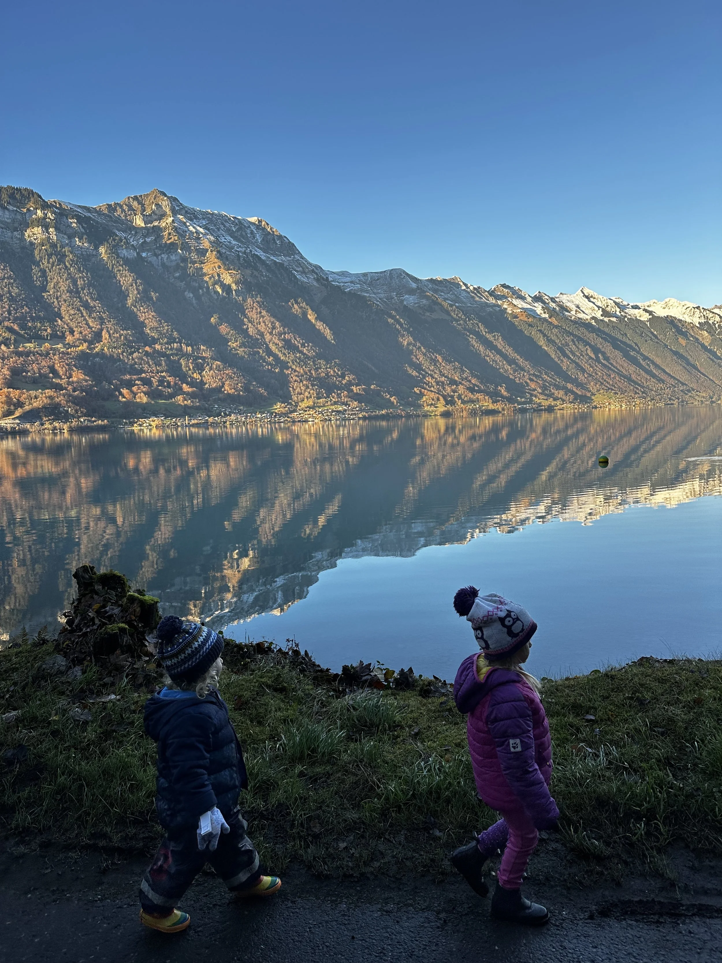 Two children in warm clothes and knit hats walking along the lakeside and mountains in the Jungfrau Region.Childcare 儿童保育 Kinderverzorging Garde d'enfants مجالسة الأطفال Cuidado de niños Присмотр за детьми Babysitiing Jungfrau Region
