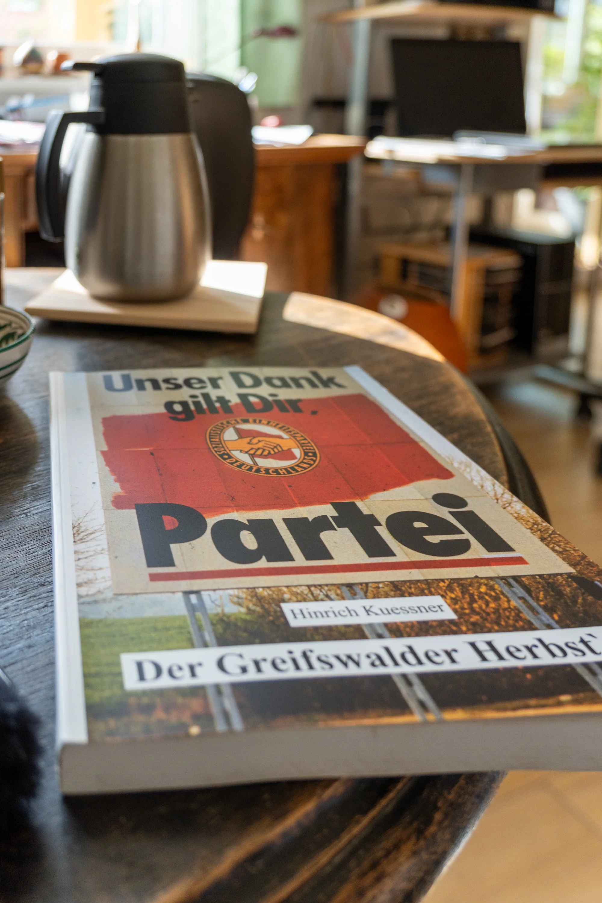 Buch „Der Greifswalder Herbst“ auf Tisch; im Hintergrund eine Isolierkanne.