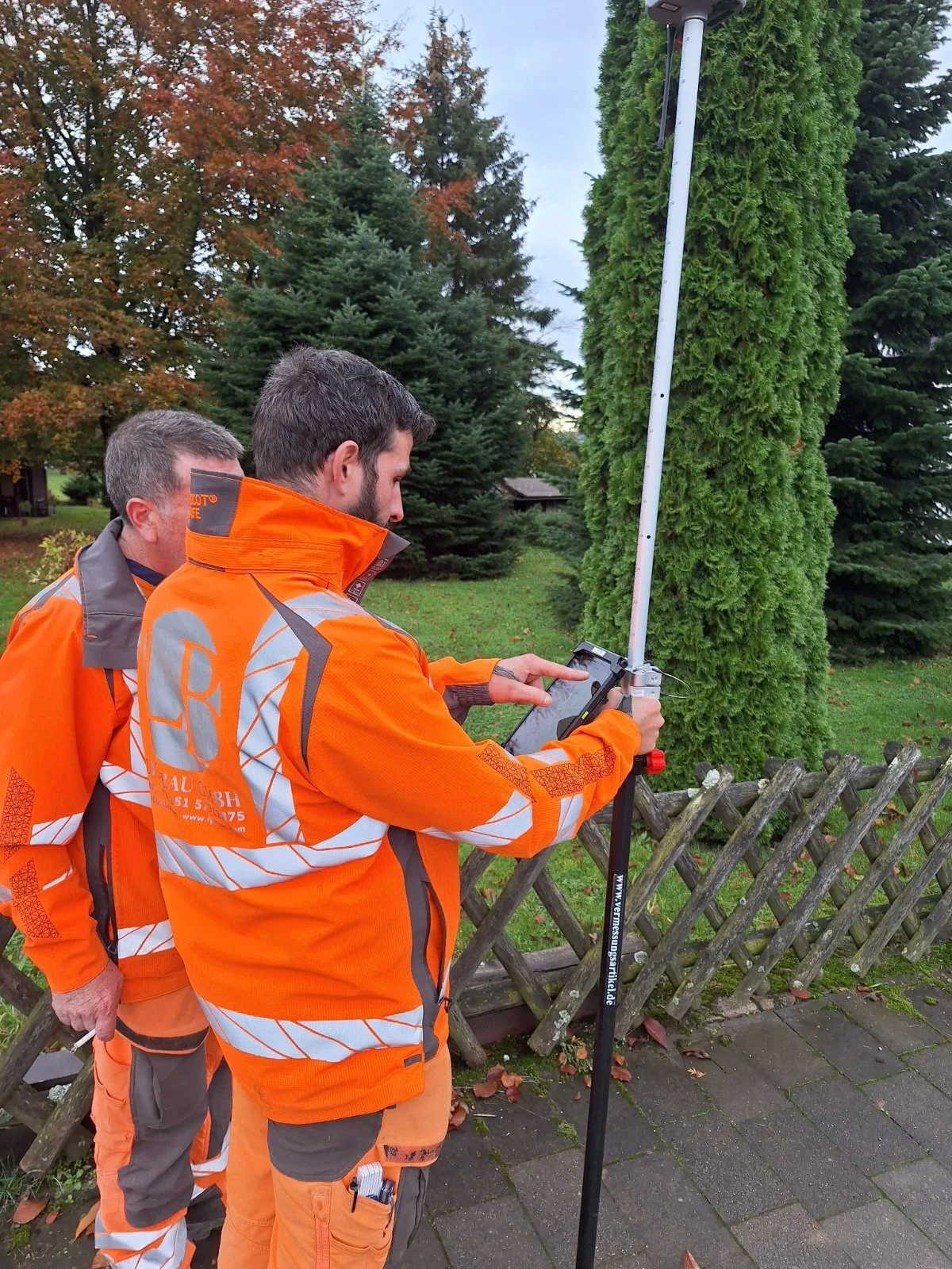 Dos trabajadores con uniforme de protección utilizando un equipo de inspección en la acera de una calle residencial.