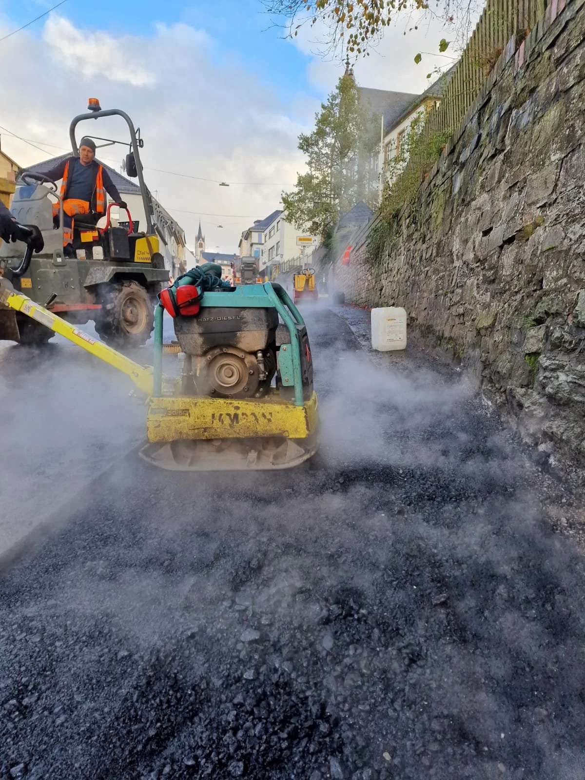 Camino en construcción con asfalto en proceso de being colocada, instrumentos de trabajo y materiales de construcción visibles.