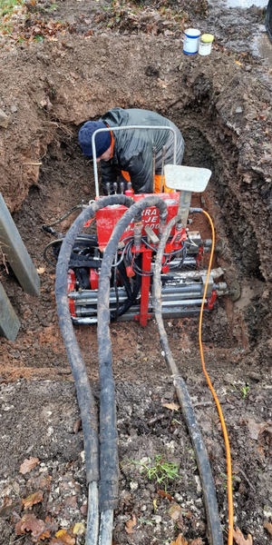 Persona trabajando en una excavación con maquinaria de perforación y tubos, con pinturas de colores en el suelo.