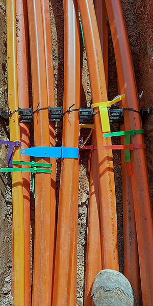 Un conjunto de tuberías de colores en gris, naranja y amarillo, aseguradas con bridas de colores azul, verde, amarillo y morado, en el suelo.