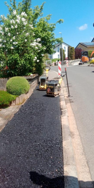 Construcción de acera con maquinaria y barandas en una calle residencial con árboles y casas