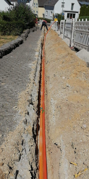 Trabajador en una obra de construcción que instala tuberías subterráneas en una zanja junto a una acera en una calle residencial.