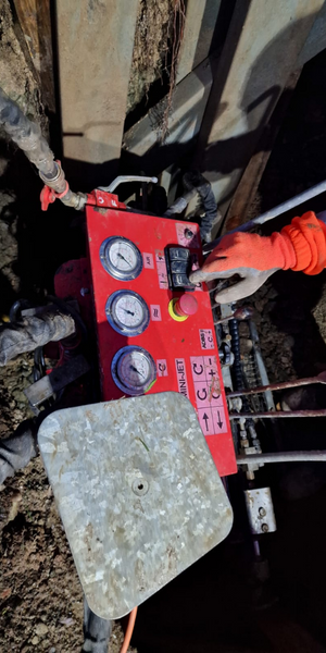 Persona operando un panel de control rojo con medidores y botones en un entorno de construcción o mantenimiento con cables y tubos.