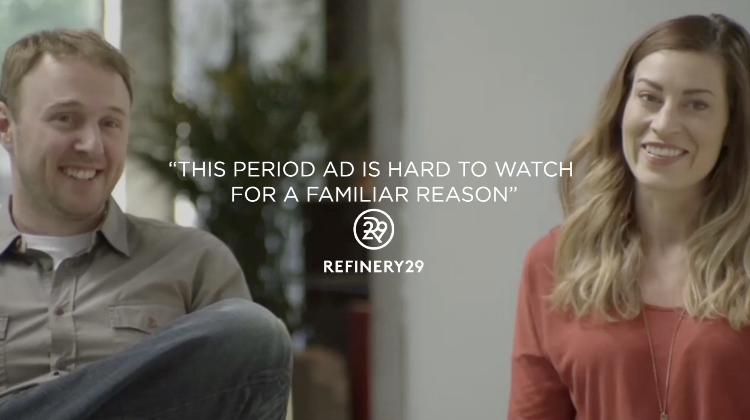 Two smiling people, a man on the left and a woman on the right, sitting indoors with a blurred background, with overlay text about an ad for Refinery29.