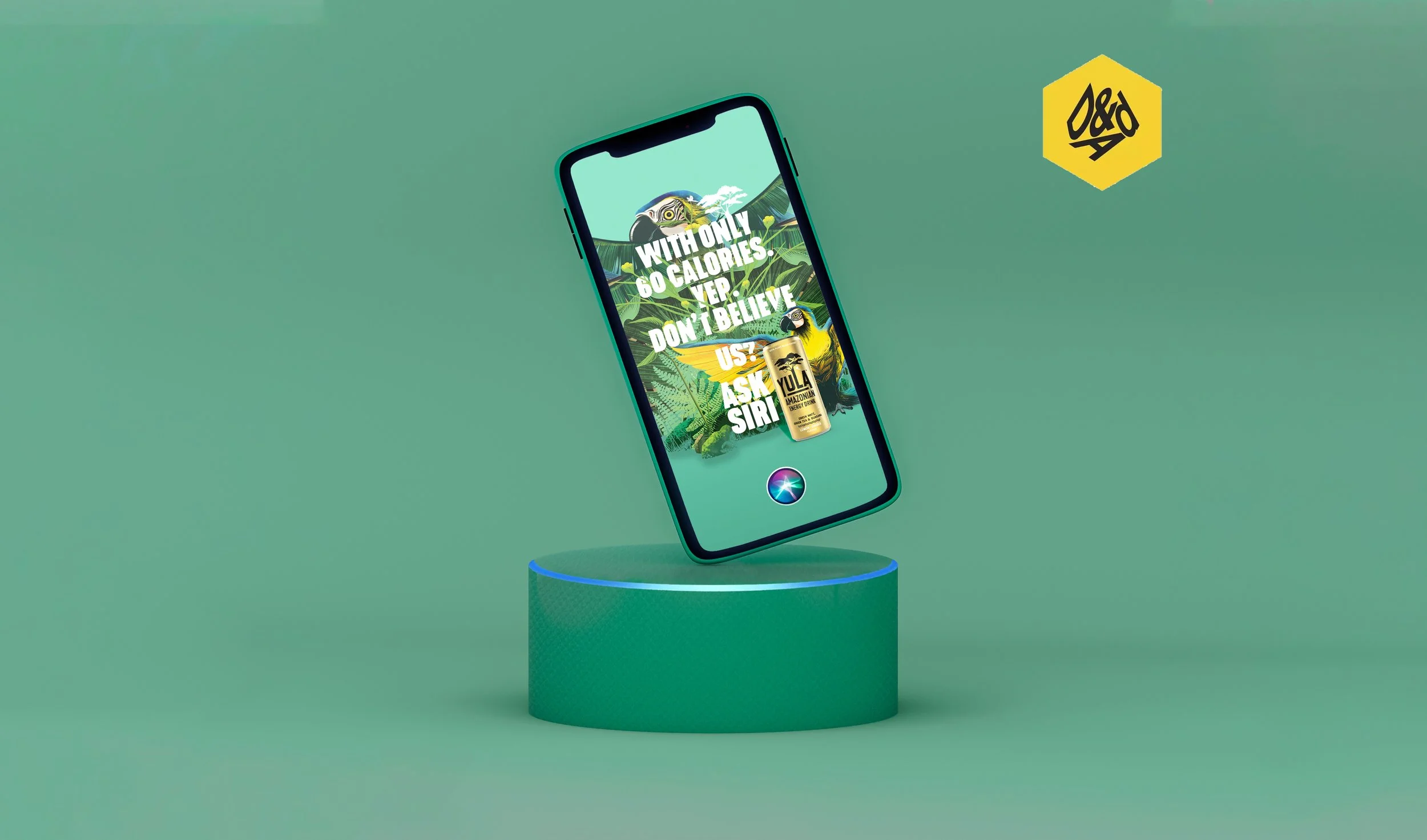 A smartphone with a vibrant jungle-themed advertisement for Yula Amazonas on the screen, featuring a toucan and tropical plants, displayed on a floating platform against a green background with a yellow hexagon logo in the top right corner.