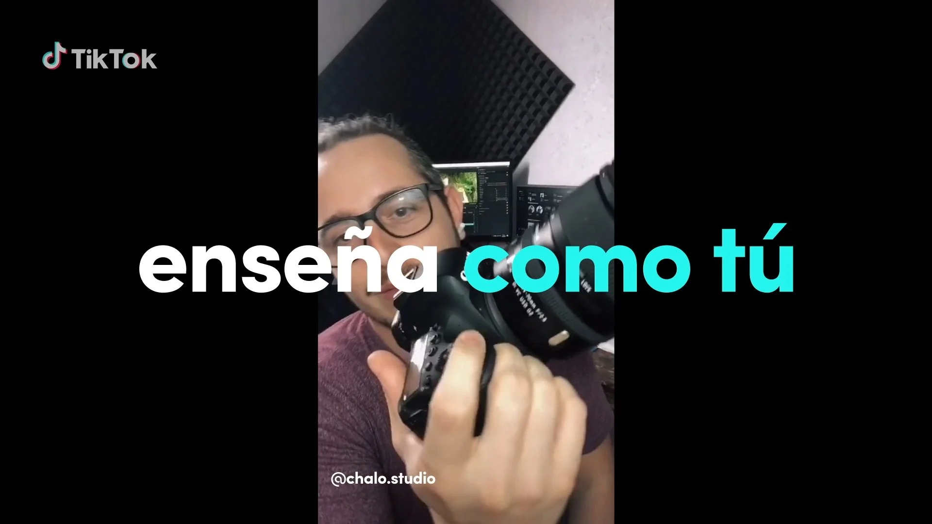 A person wearing glasses holding a camera, with a microphone in front, and a computer monitor in the background. Overlaid text says "enseña como tú" in large letters.