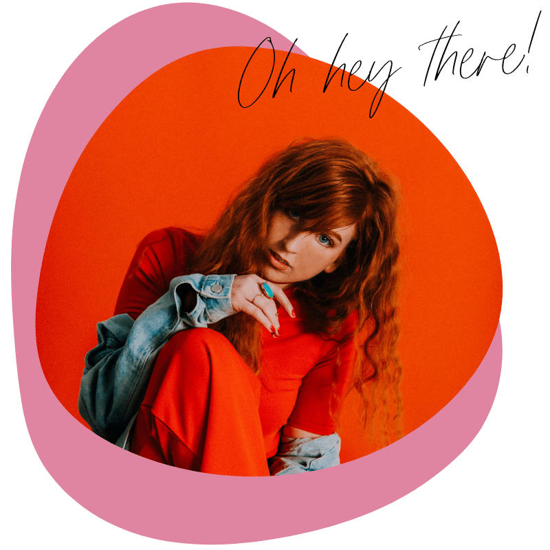 A woman with long, curly red hair wearing a red outfit and a denim jacket, posing against an orange background with a pink abstract shape around her and the text "Oh hey There!" written in black cursive.