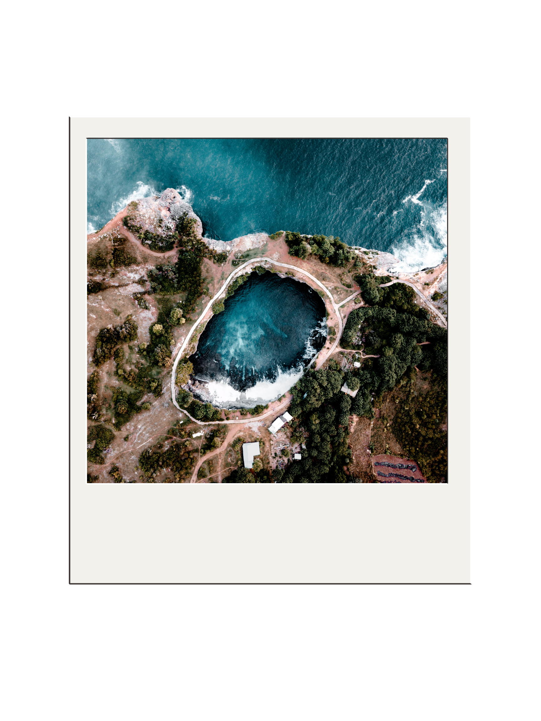 Aerial view of a natural water formation with a small waterfall, surrounded by trees and paths, near the ocean.