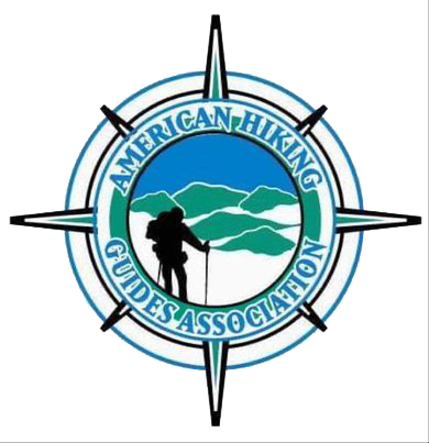 Logo of the American Hiking Guides Association featuring a hiker silhouette and mountain landscape encircled by a compass design.