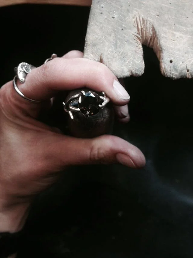 Person holding a ring with a large black gemstone, with a stone carving of a bird in the background.