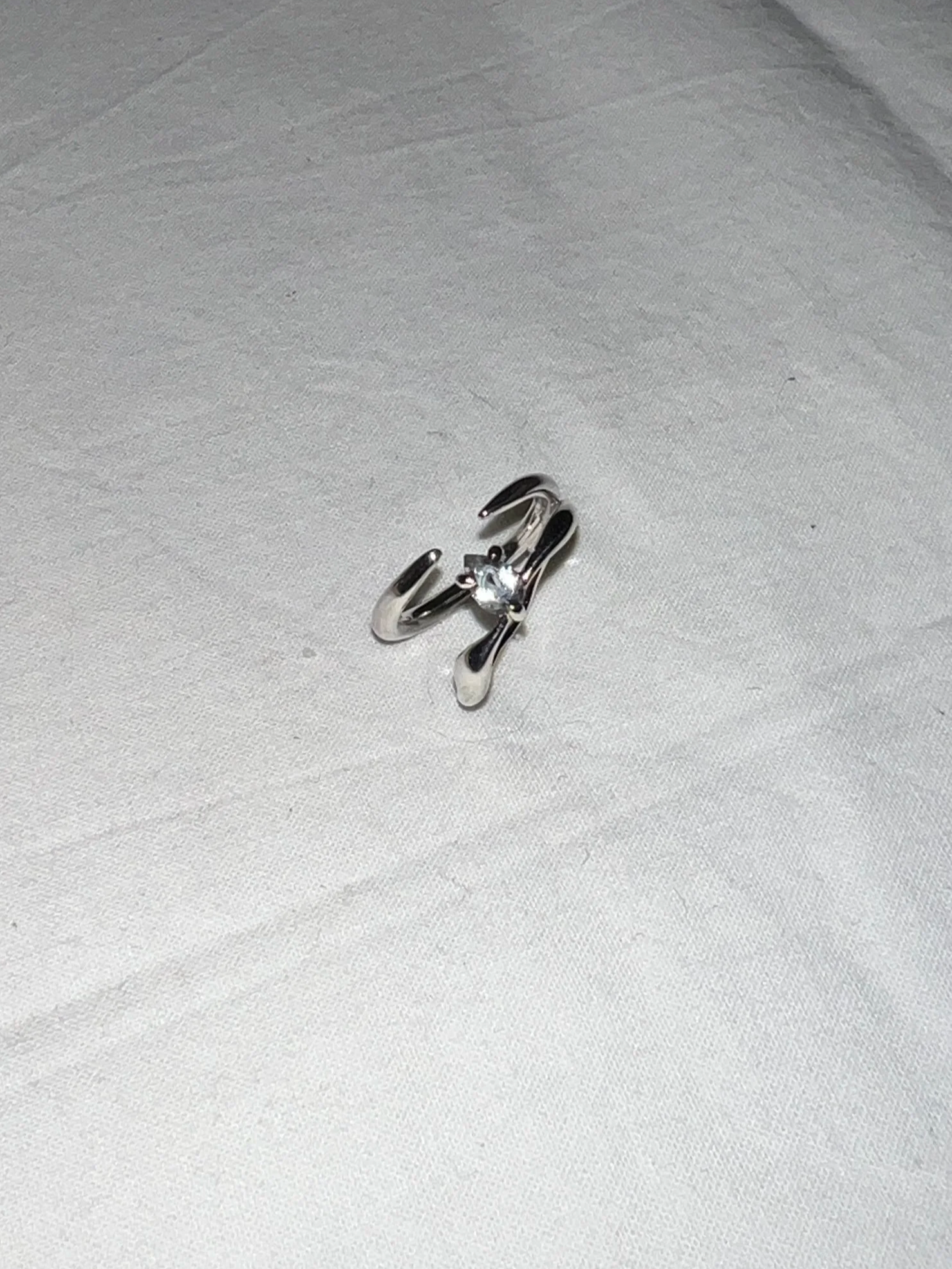A silver ring with a small gemstone on a white fabric surface.
