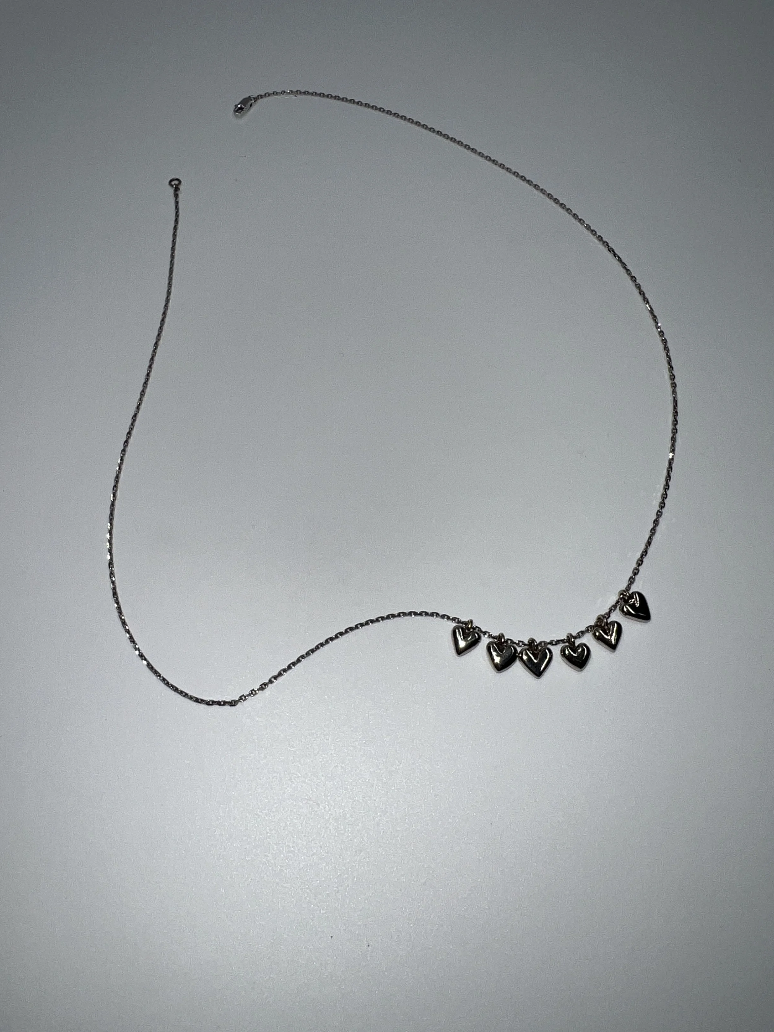 A silver necklace with seven small heart charms laid out on a plain white surface.