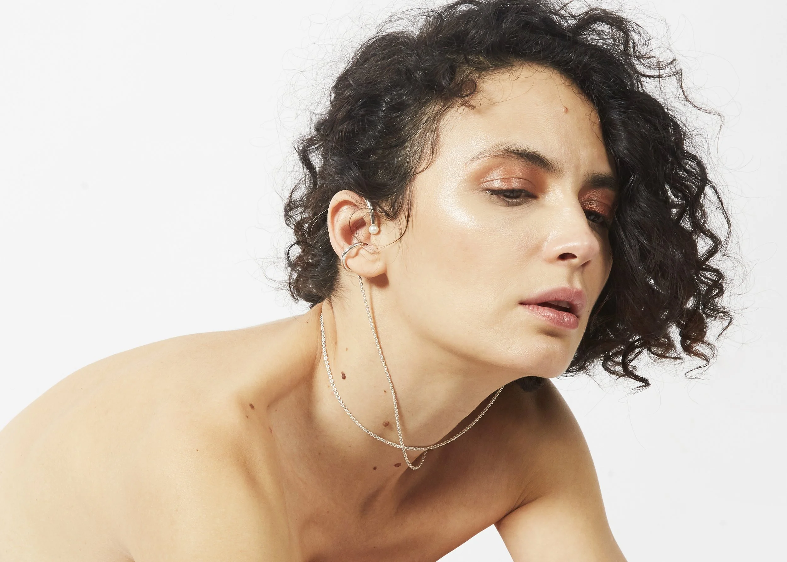 A woman with short curly hair wearing layered silver jewelry with a white background.