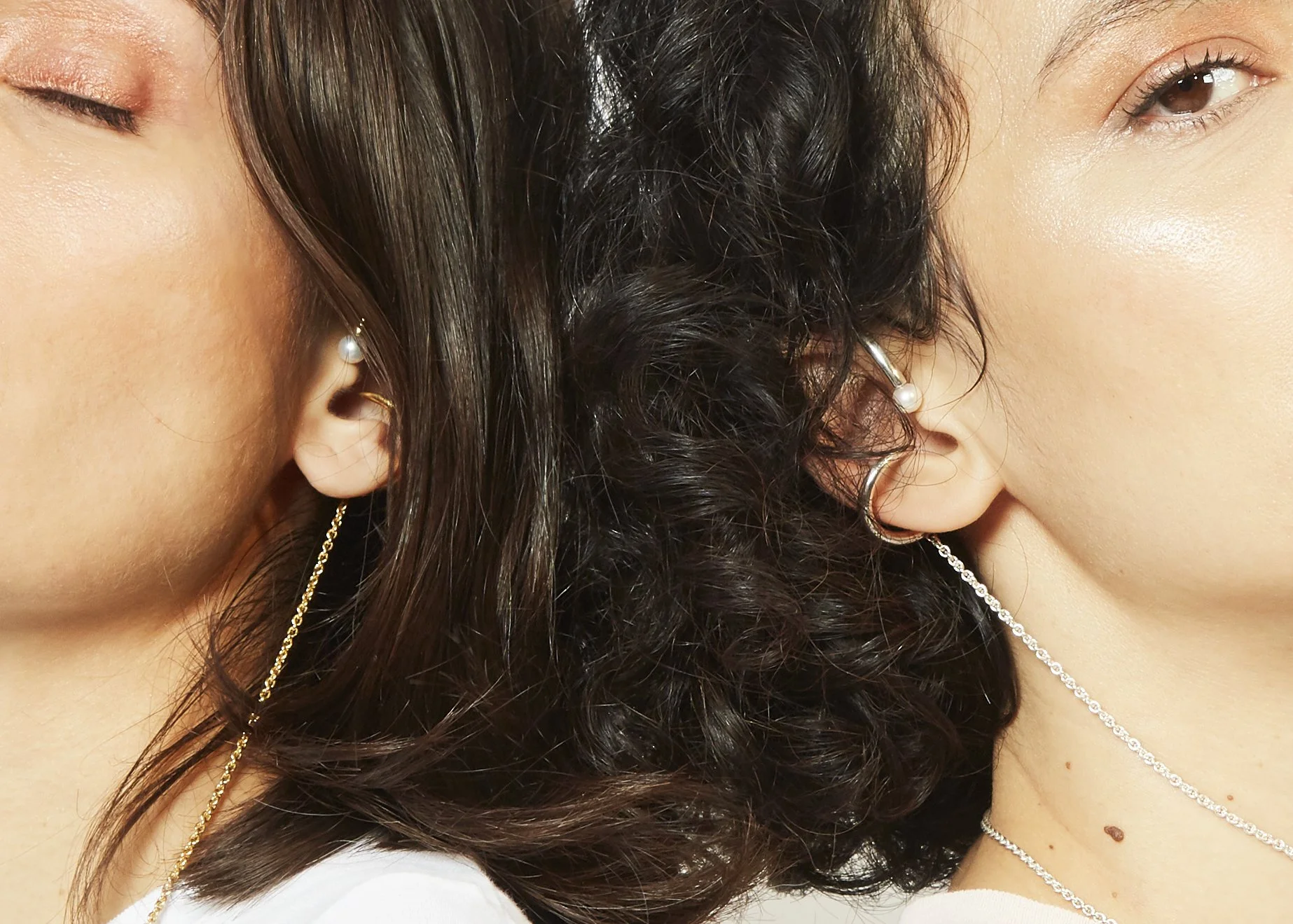 Close-up of two women showcasing their earrings and necklaces with their faces positioned back-to-back.