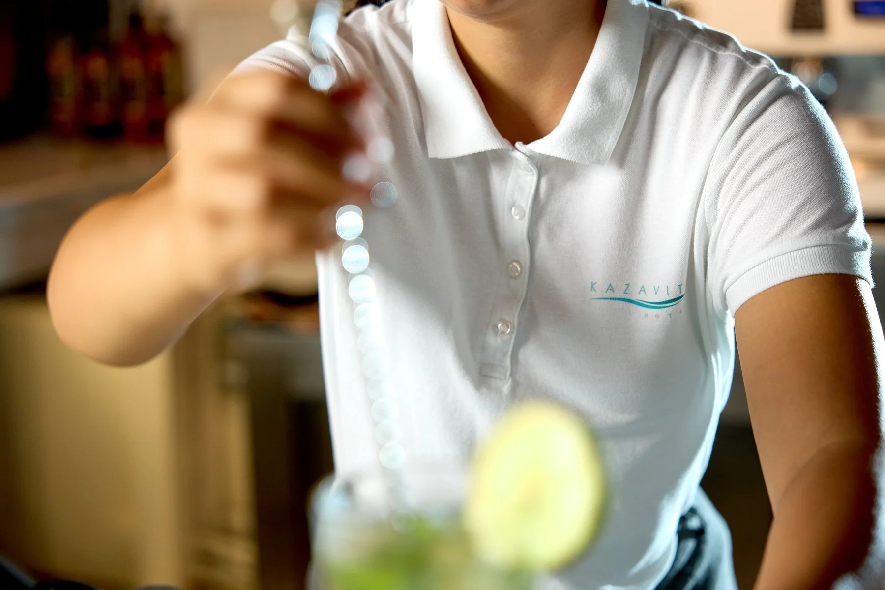 Barista in white polo shirt preparing a drink with lime slices in a cafe.