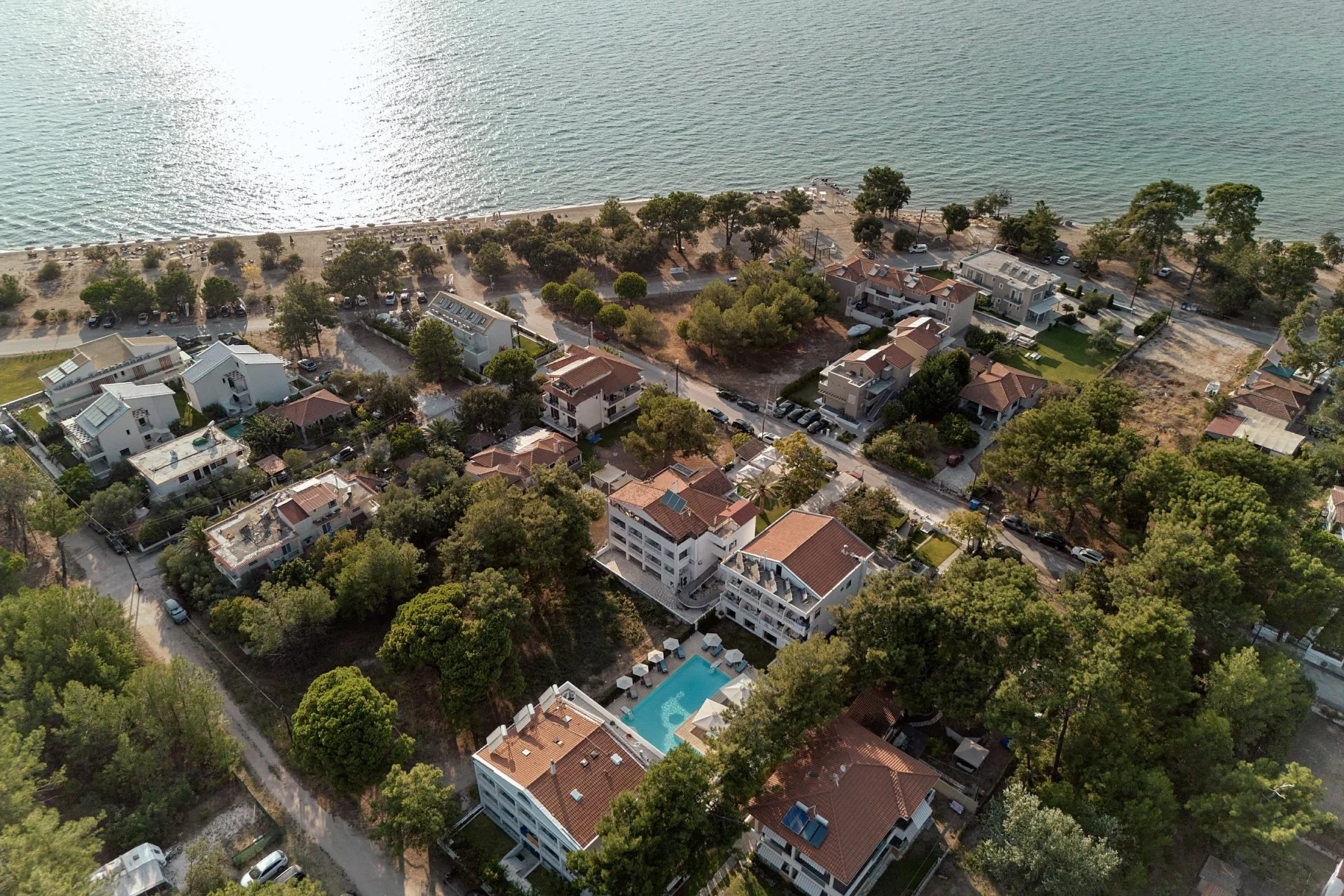 Aerial view of a coastal neighborhood with houses, trees, a swimming pool, and a beach along the water.
