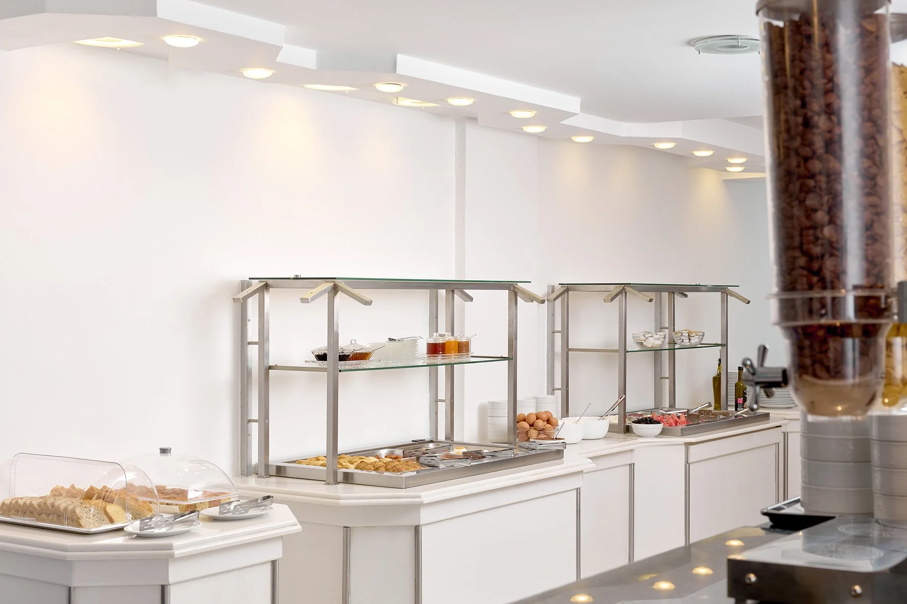 Buffet area with food and beverage items, including pastries, eggs, syrup, and cereal, in a clean, well-lit setting.