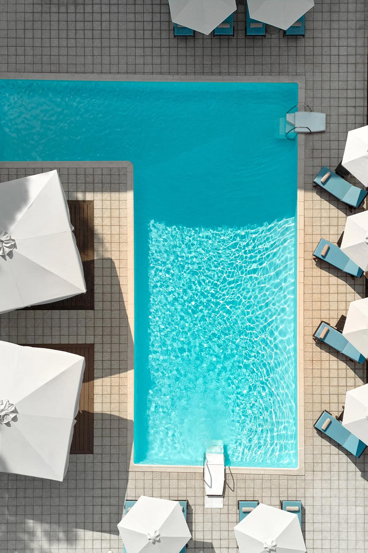 An aerial view of a swimming pool surrounded by poolside lounge chairs with white umbrellas.