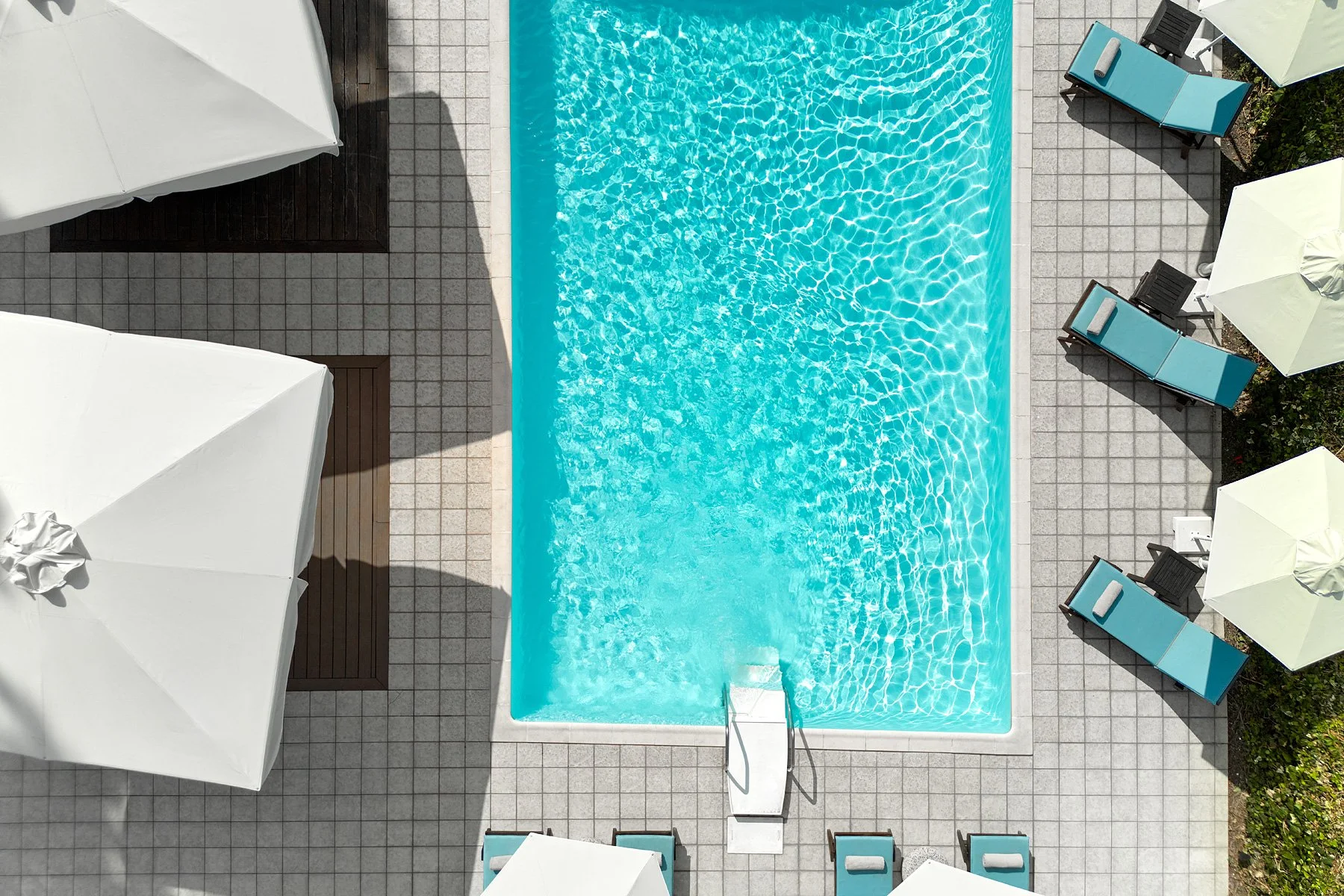 Aerial view of a swimming pool surrounded by lounge chairs with blue cushions and umbrellas.