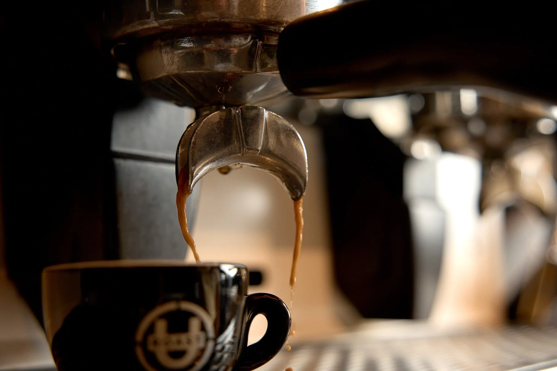 Close-up of an espresso machine pouring coffee into a black mug with a logo on it.