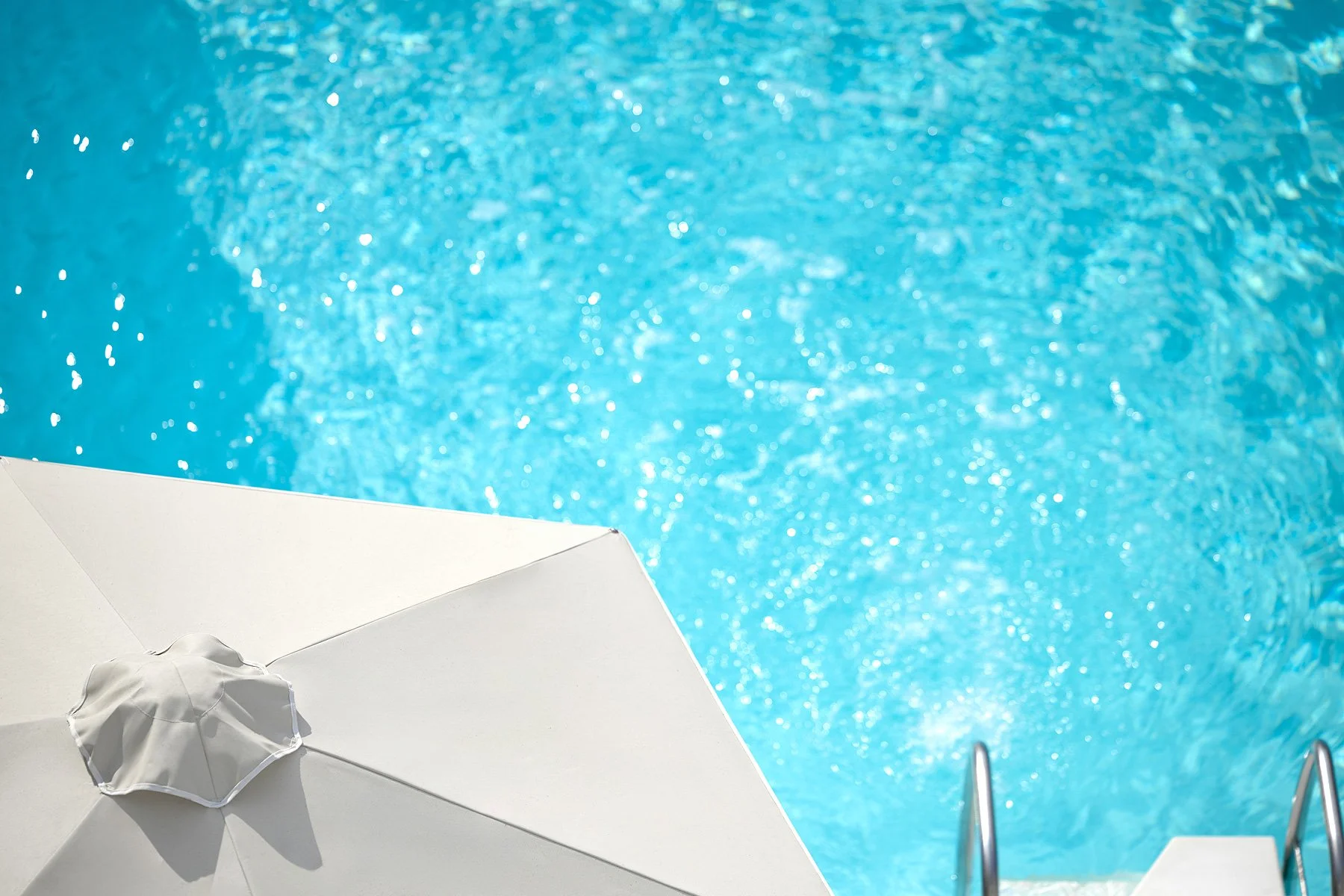 Swimming pool with blue water, white pool steps, and a white umbrella at the poolside.