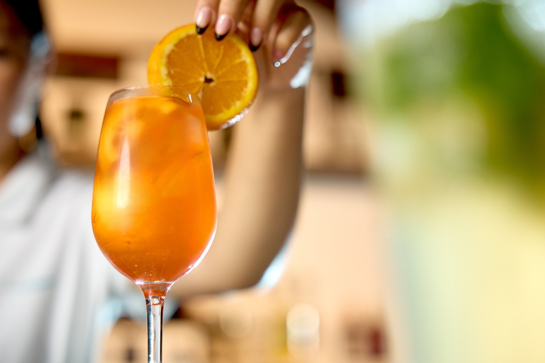 A person placing a slice of orange on the rim of a tall glass filled with orange-colored beverage