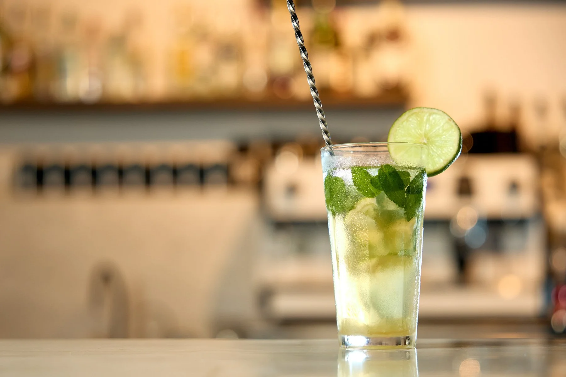 A tall glass of lemonade garnished with mint leaves, lime slices, and a lime wedge, with a striped straw inside.