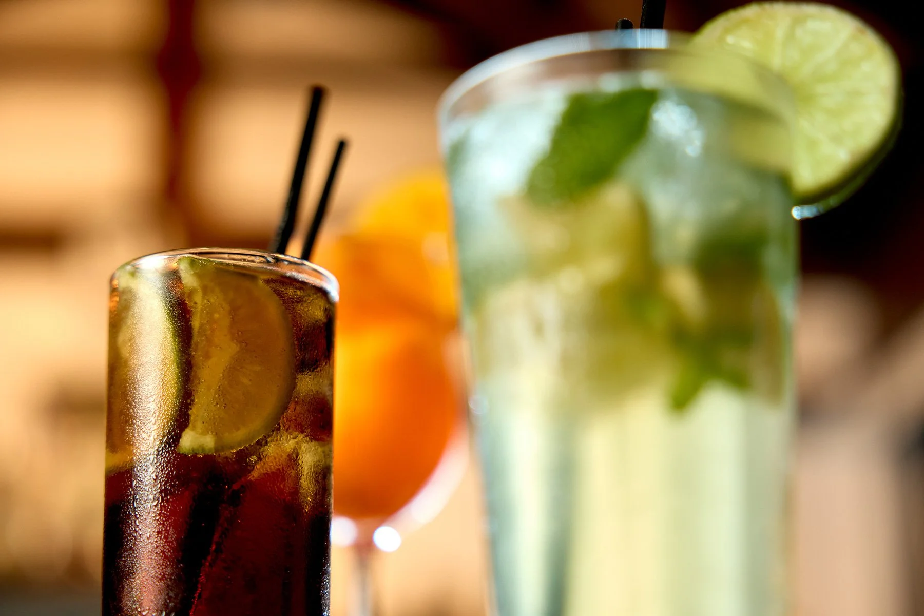 Three colorful cocktails with lime and fruit garnishes, with a blurred background.