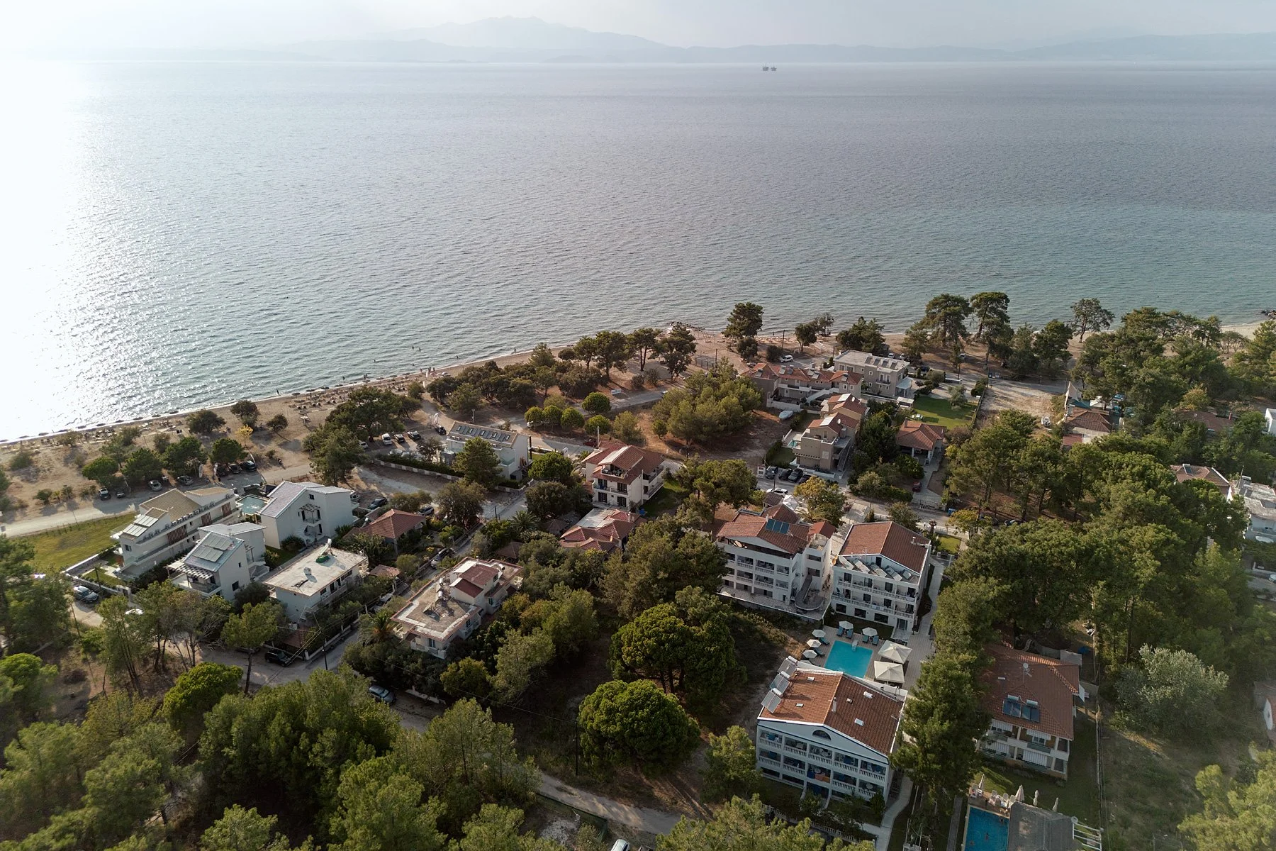 Aerial view of a coastal neighborhood with houses, trees, and a beach near a large body of water.