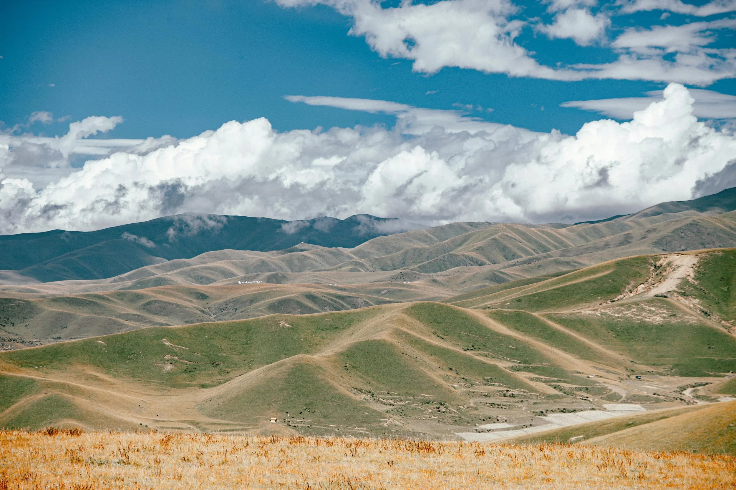Scenic view of green rolling hills with mountains in the background under a partly cloudy sky.