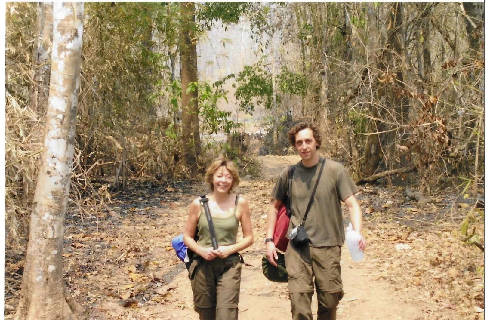 Twee mensen, Martine & Rudi, de oorspronkelijke founders van bar & restaurant Mosquito Coast in Gent, wandelen door een bos, omringd door bomen en bladeren, op een stoffig pad.