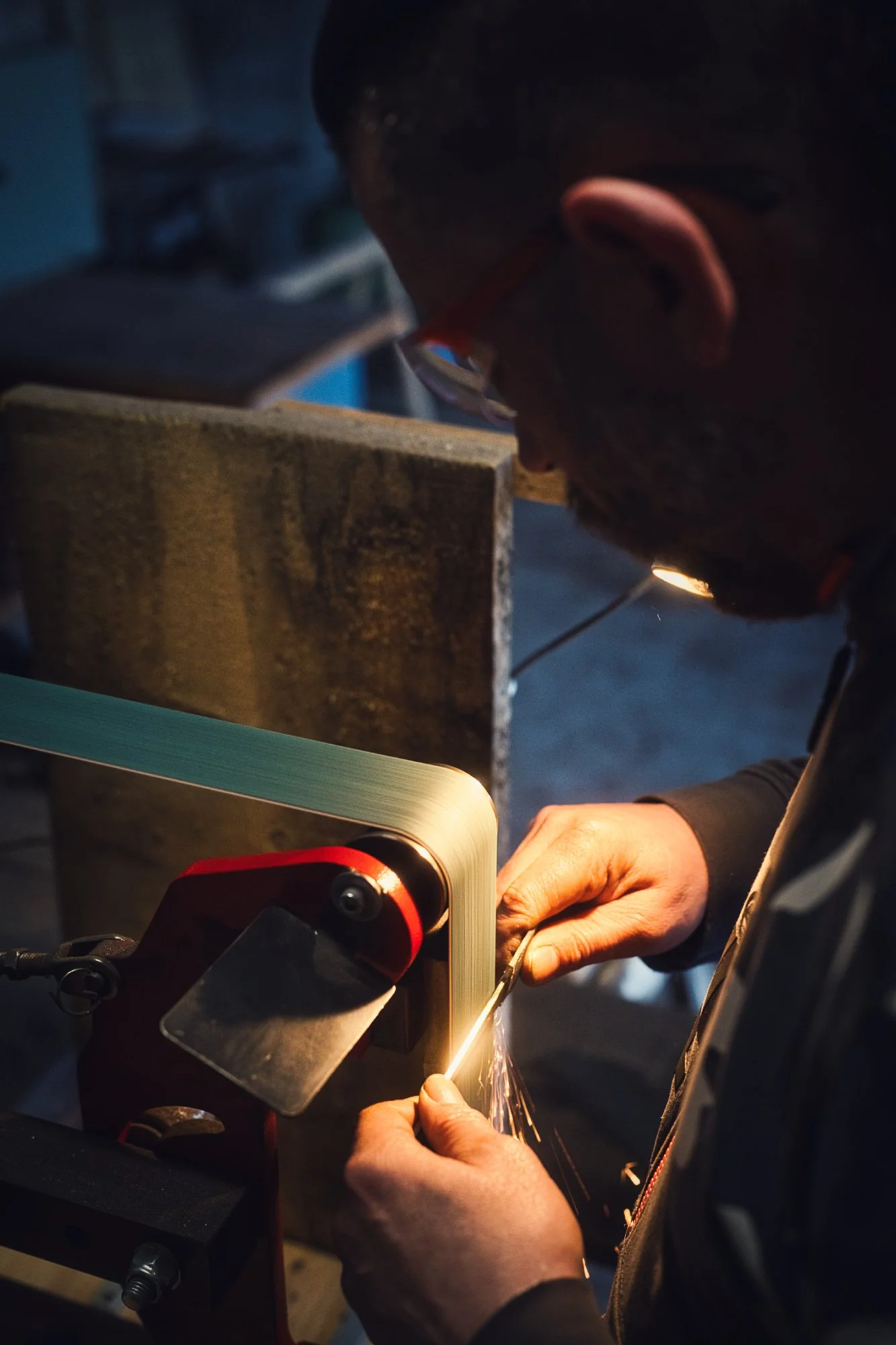 Homme qui lime une lame de couteau sur une machine à bande. Photo de la Forge du Ragnarok.