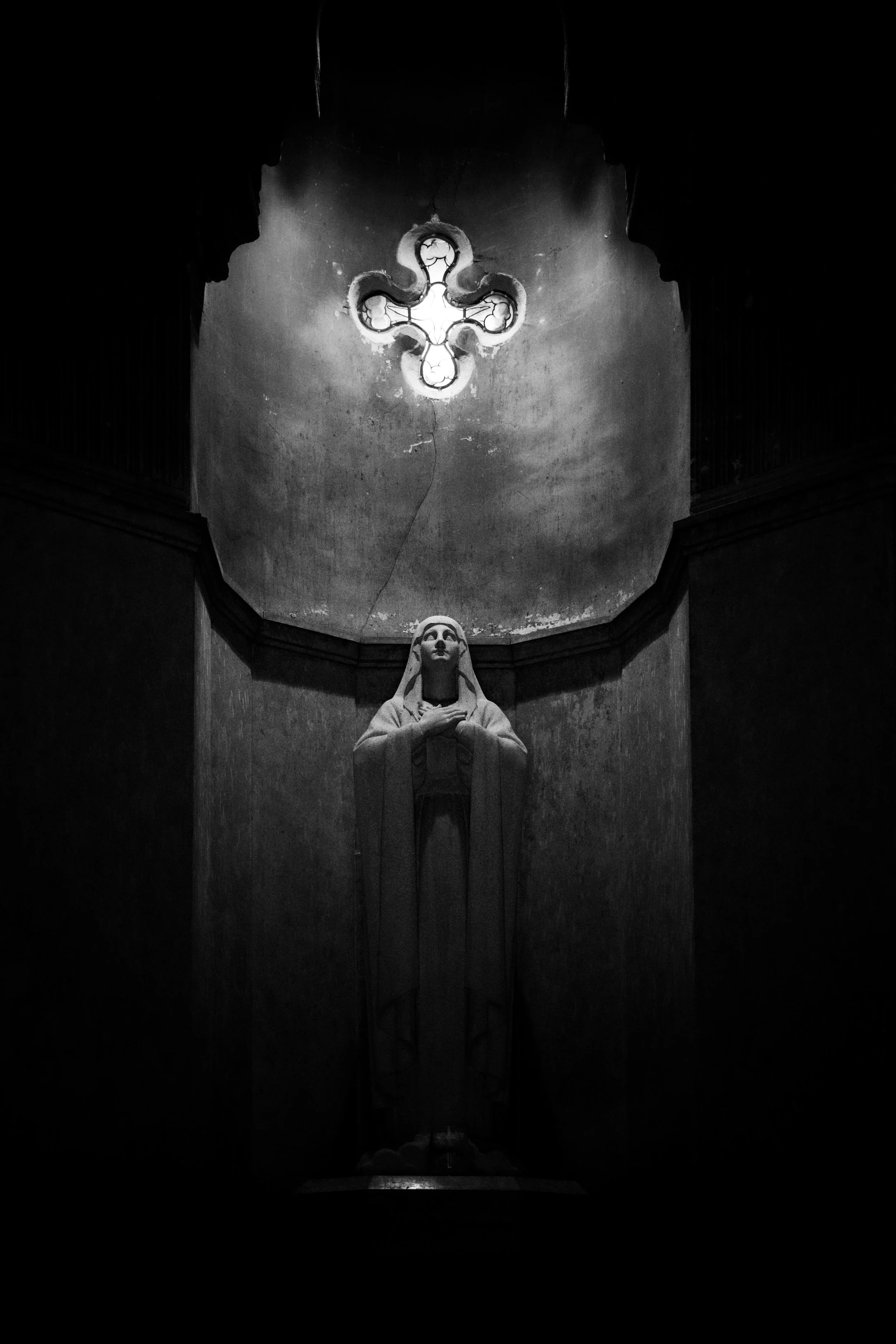 Une statue de la Vierge Marie dans l'église de La Ferté-Macé avec un plafond en coupole illuminé par une lumière provenant d'un trou en forme de croix.
