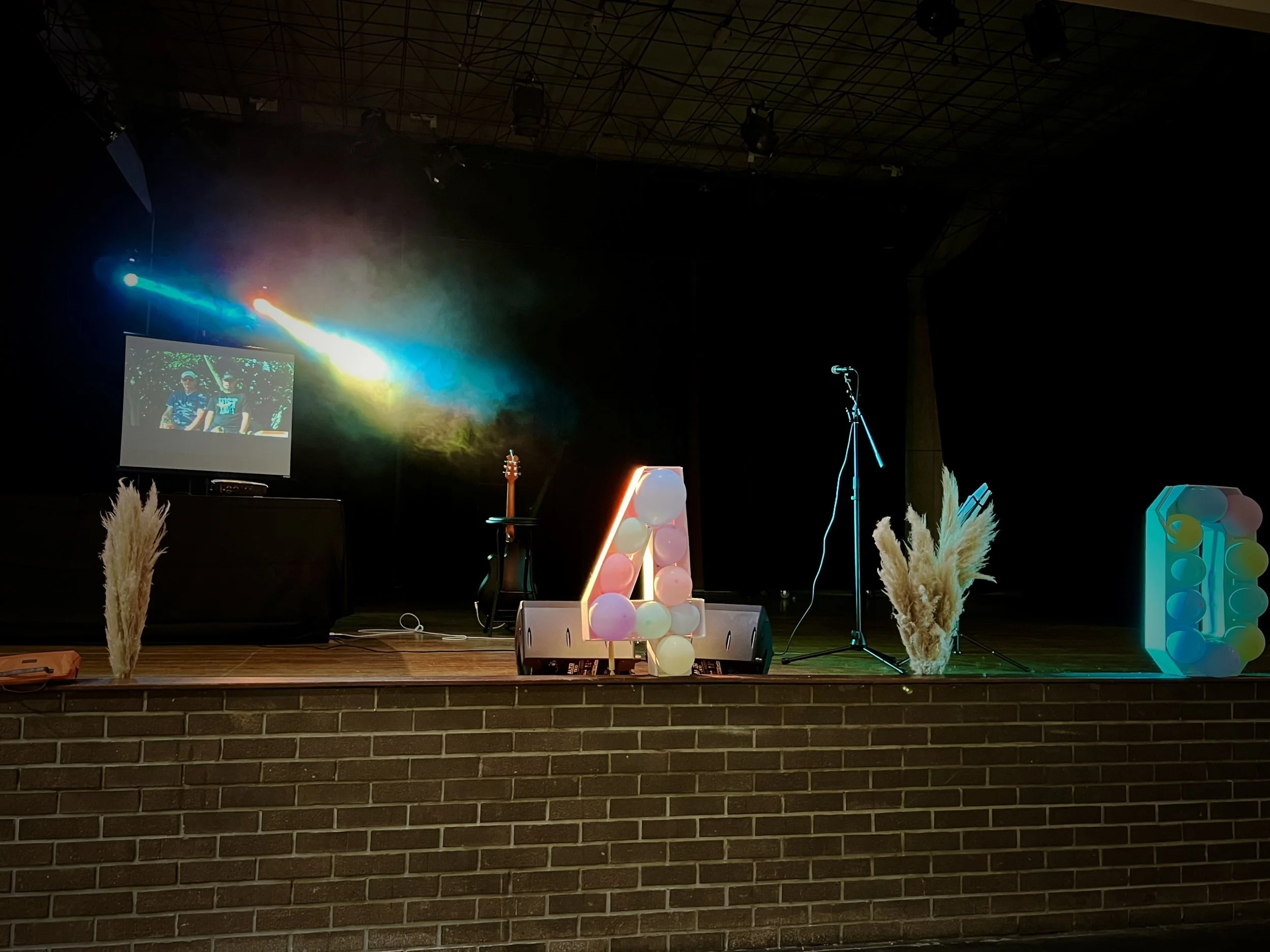 Scène d'un anniversaire avec éclairage, un micro et guitare, et un écran vidéo à gauche avec diffusion de vidéos personnalisés.