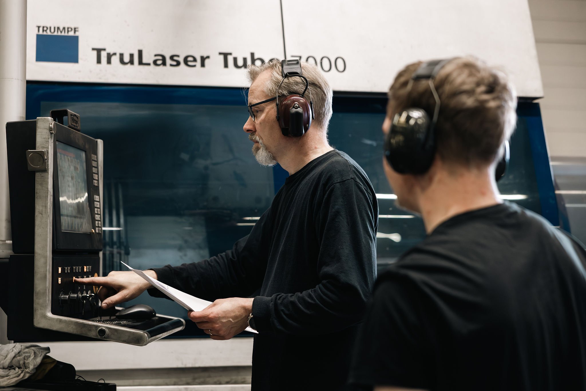Työntekijät käyttämässä putkilaserkoneen ohjauspaneelia teollisuushallissa.