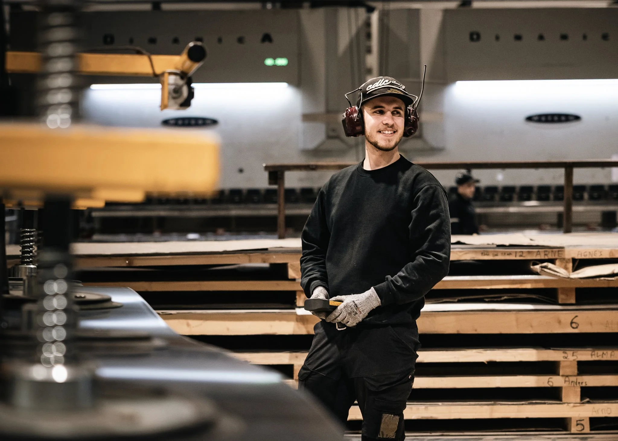 Työntekijä teollisuushallissa kuulosuojaimet päässäohjaamassa  alipainenostinta.