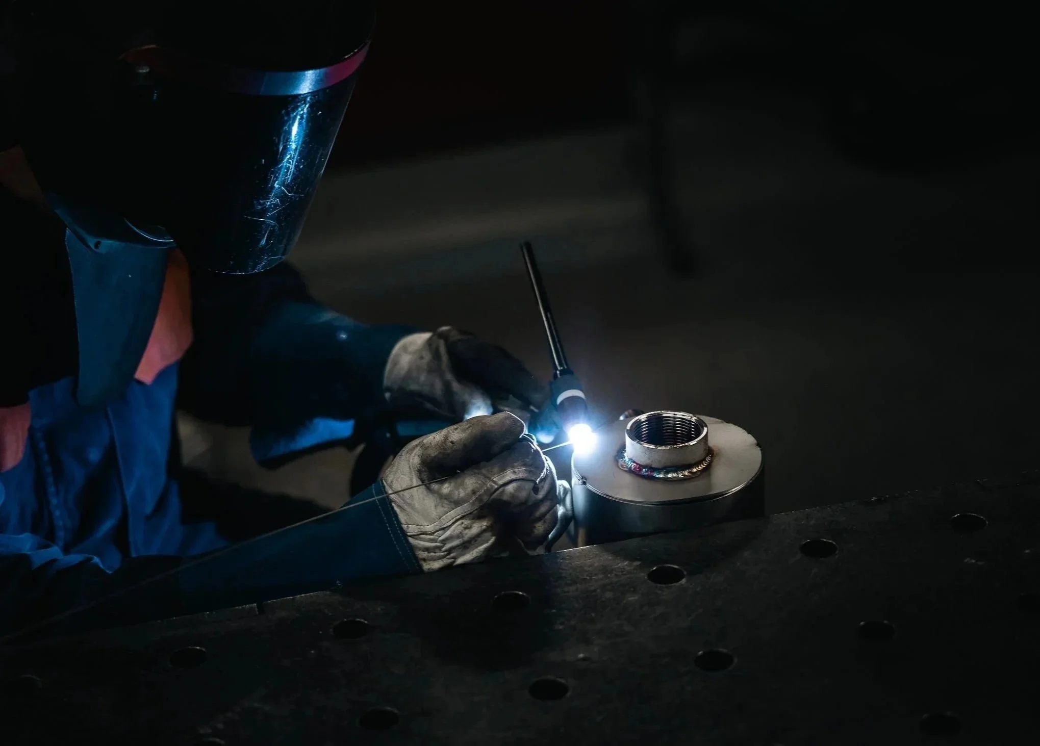 Hitsaaja työskentelemässä valokaaren kanssa metalliosan parissa suojavarusteet päällä..