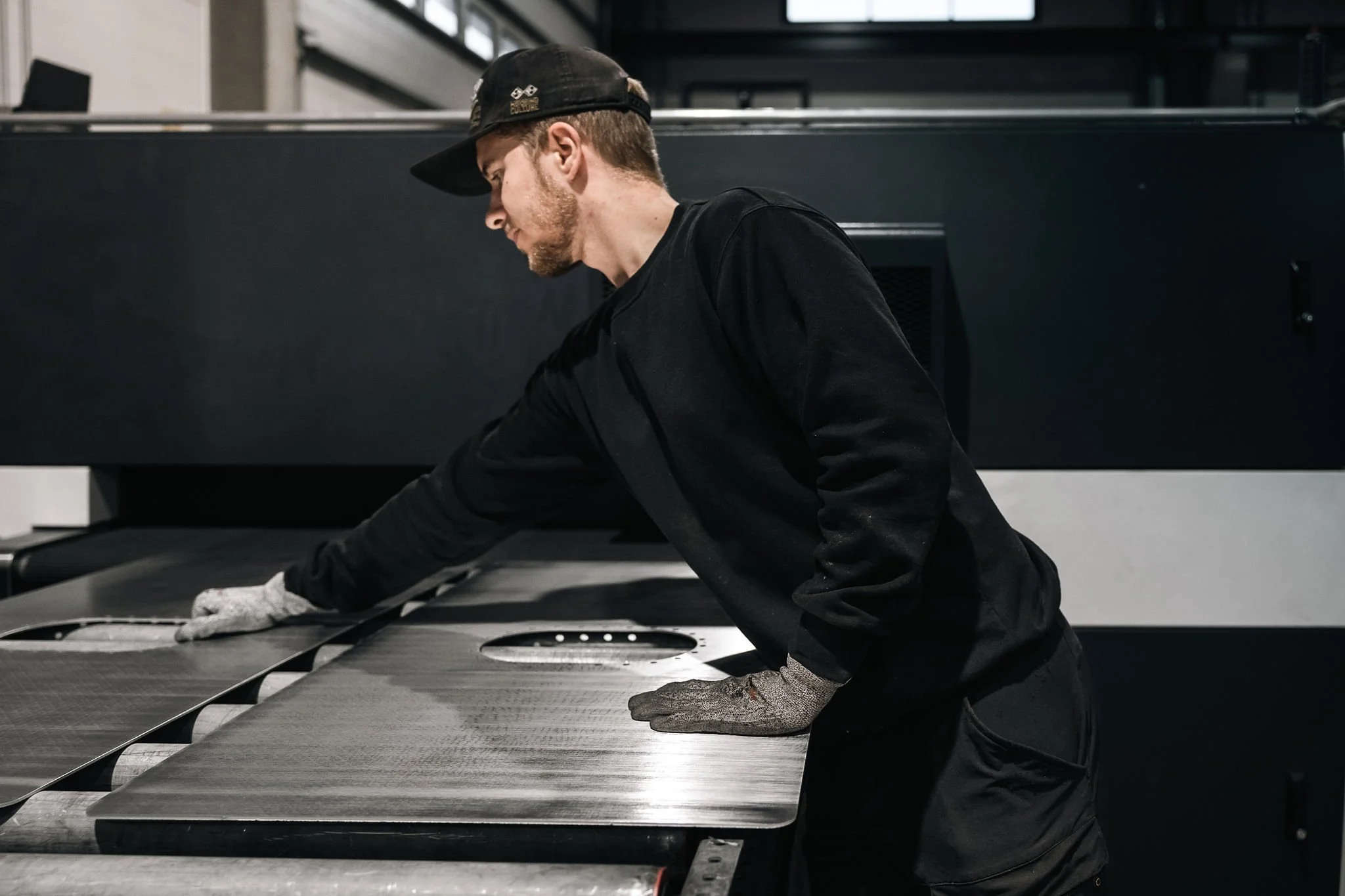 Työntekijä ohjaamassa viimeisteltyjä metallilevyjä koneelta ulos