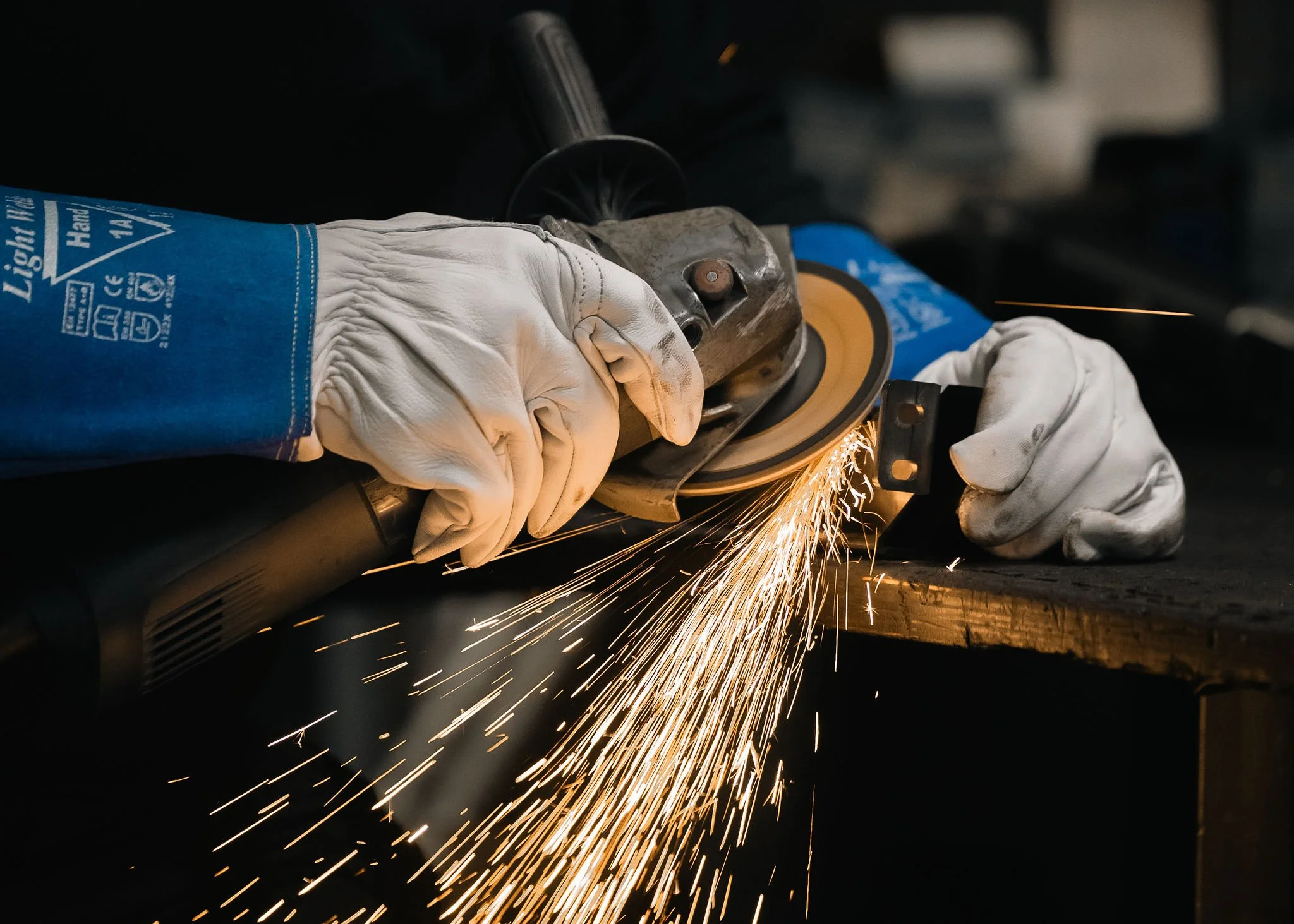 Työntekijä hiomassa metalliosaa kipinöiden lennellessä.