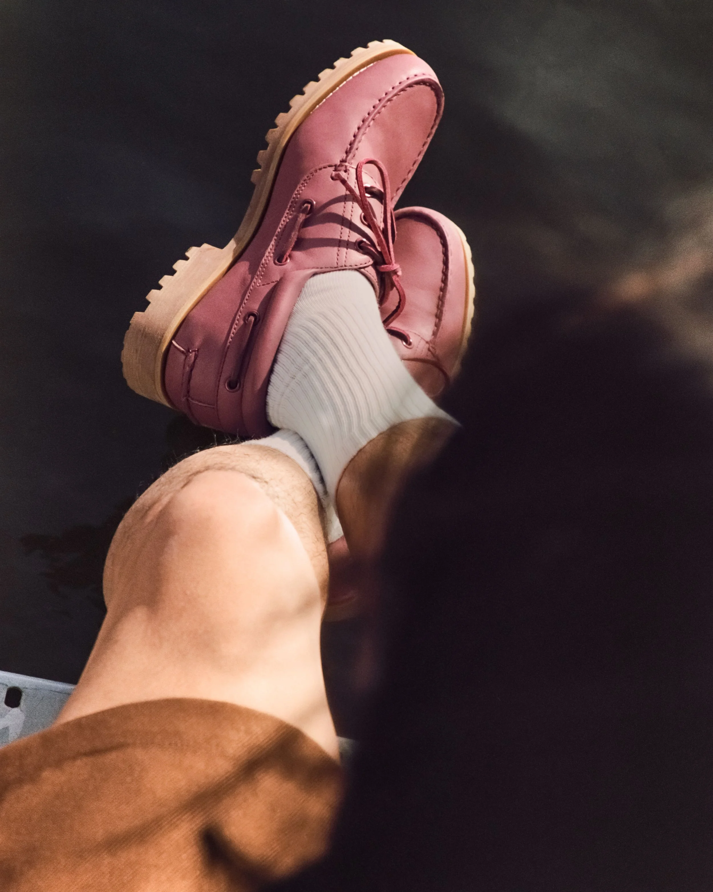 A person wearing pink leather boots, white socks, and brown shorts, with their feet up on a dark surface.