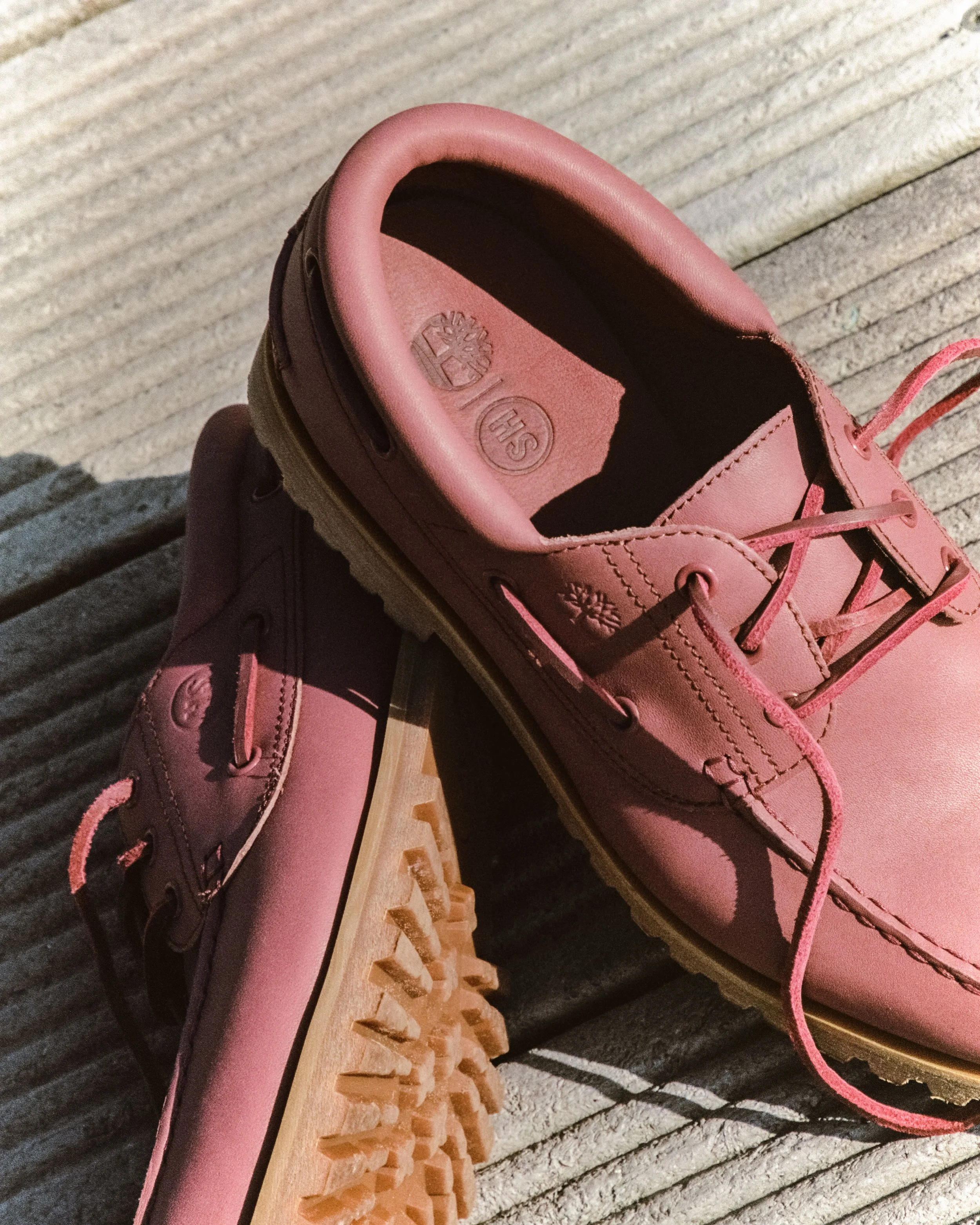 Close-up of pink Timberland boat shoes with laces and rugged tan soles, resting on a textured wooden surface.
