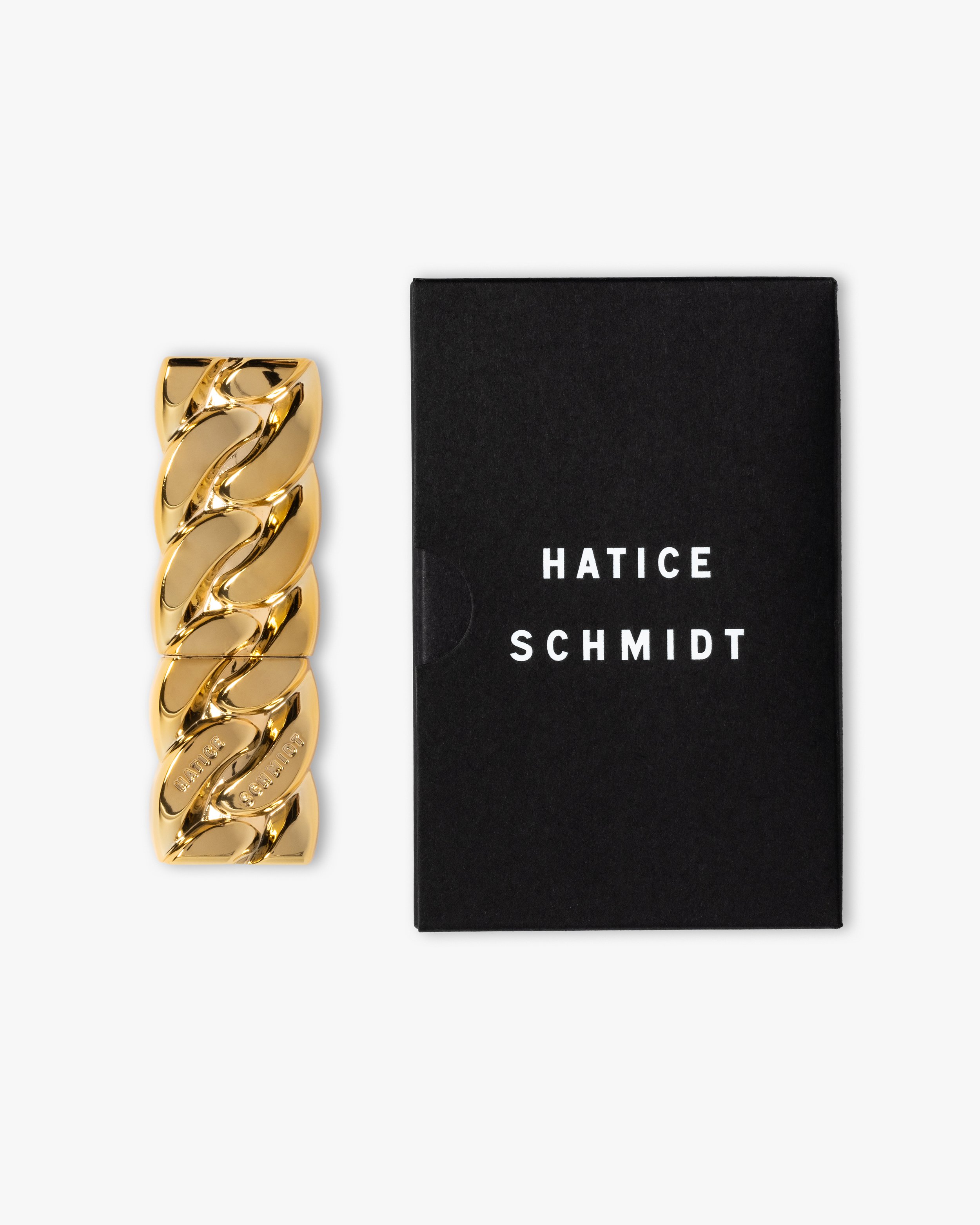 Gold chain link bracelet with engraved branding next to a black box with white text reading 'HATICE SCHMIDT'.